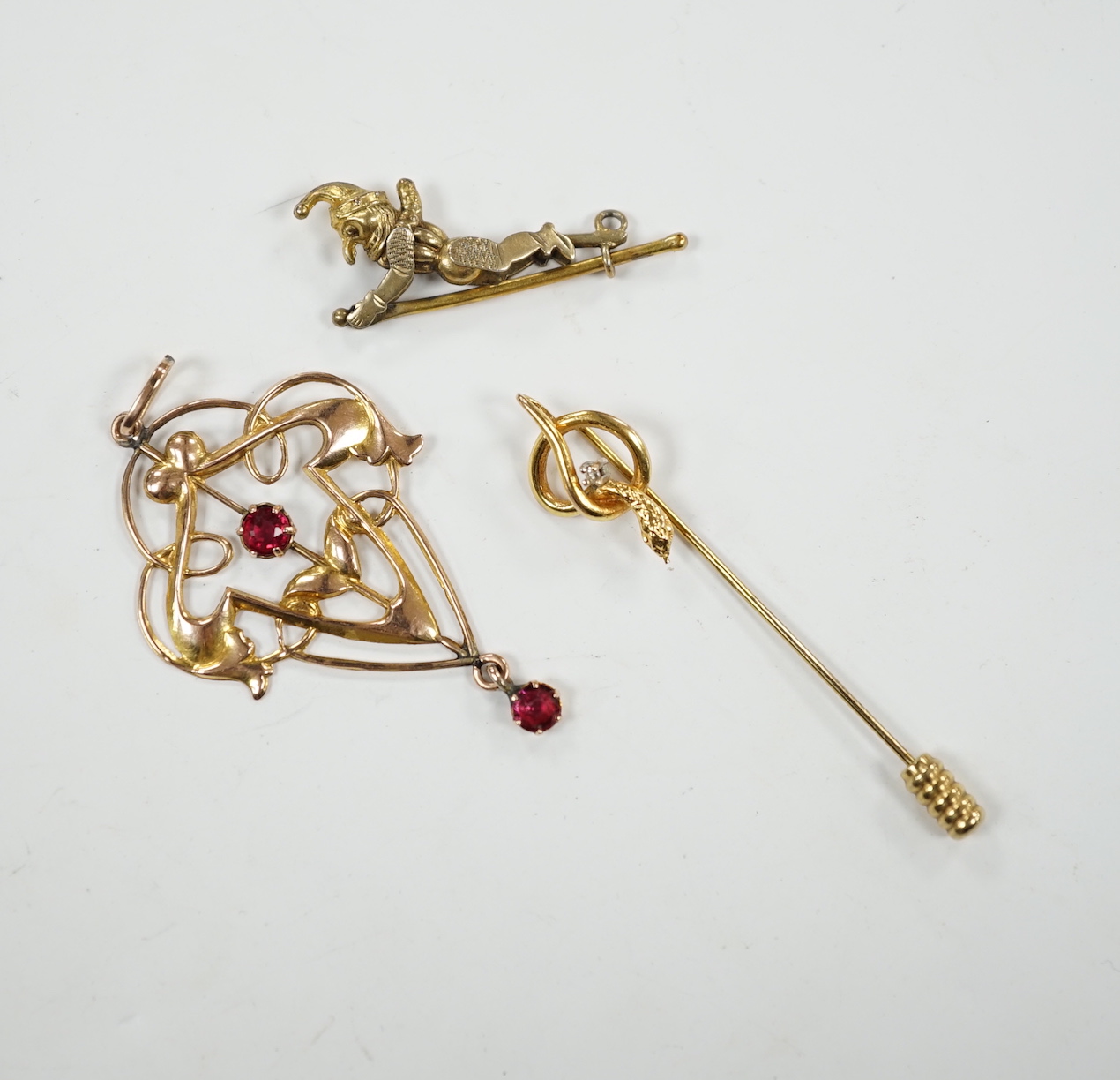 An Art Nouveau yellow metal and two stone gem set drop pendant, 53mm, an articulated Mr Punch charm and a modern 9ct gold and diamond chip set serpent stick pin.